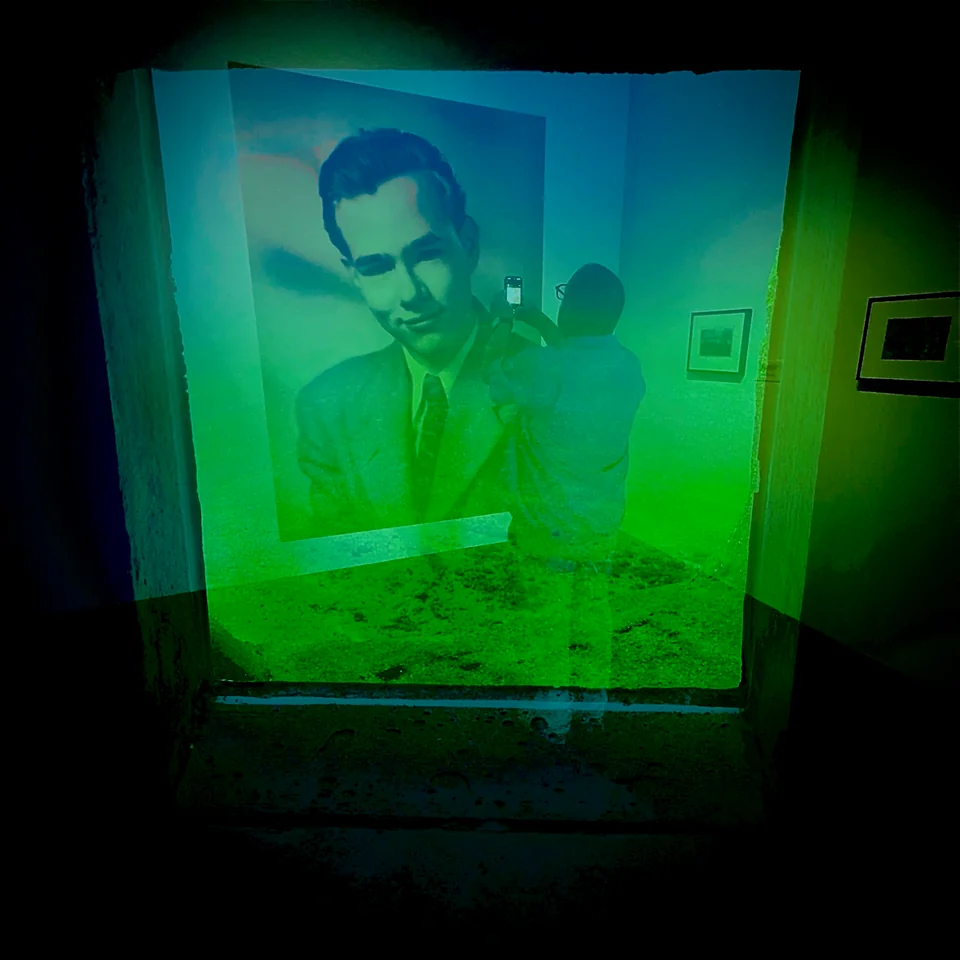A framed portrait layered with a museum visitor in blue and green light.
